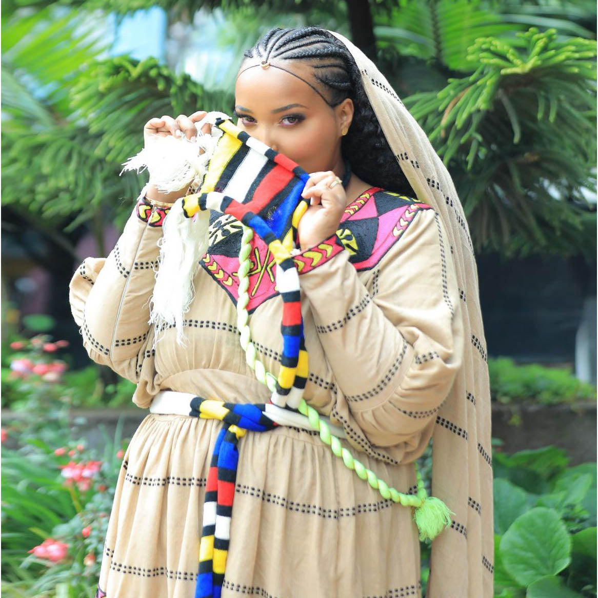 Woman in traditional attire with colorful accessories standing outdoors. Ashenda-inspired Ethiopian clothing