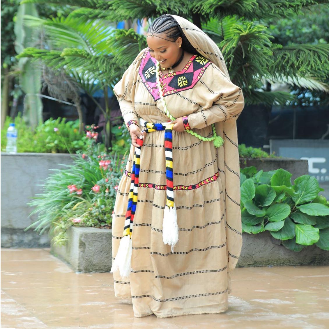 Woman in traditional attire with colorful accessories standing outdoors. Ashenda-inspired Ethiopian clothing